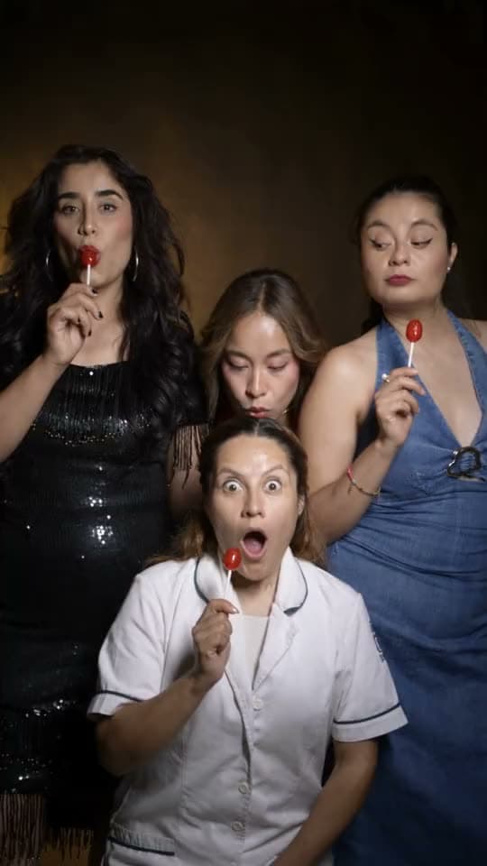 Cuatro actrices con paletas se secretean y se ríen frente a la cámara